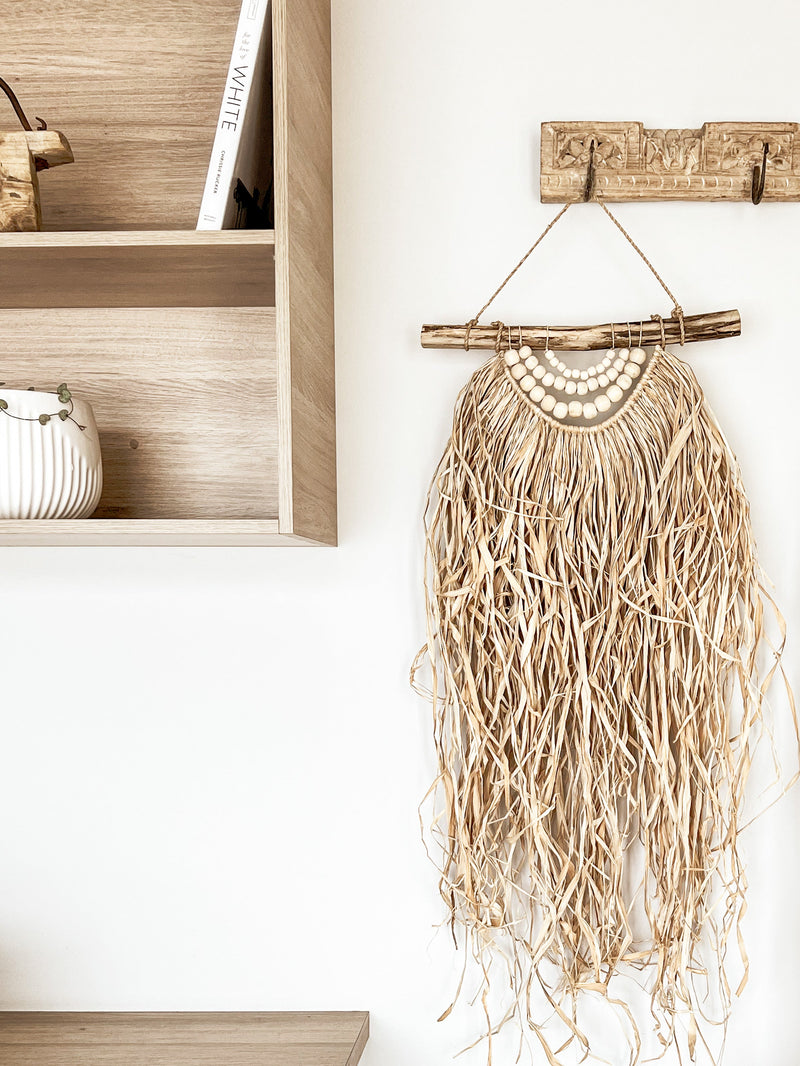Timber beaded garlands & a waterfall effect of weaved raffia freely cascading from a natural driftwood base.   The Mani wall hanging is a popular choice for use on an entrance wall hook, or filling an empty space around your home. With its raw coastal feel & naturally rustic materials, this hanging is ideal for adding an effortless statement to any interior space. 