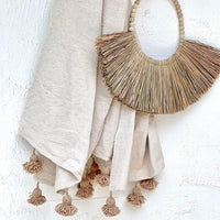 Raw timber beads over a teardrop hoop base, housing a natural alang alang seagrass skirt. The Ivana is a unique, handmade & neutral piece that compliments its surroundings with raw textures and modern boho elements.  Hang from a wall hook in a bedroom, living or alfresco area to add a villa style aesthetic to your space.   Dimensions: 70cm tall x 85-90cm wide  Natural Seagrass will lighten over time if exposed to direct sunlight. Please consider this before hanging your piece.