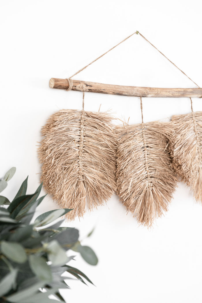 A trio of hand braided raffia leaves hang from a natural driftwood piece found by the coast & completed with a Jute hanger. This wall hanging is ideal for those who love raw texture & the feel of natural materials in their home.