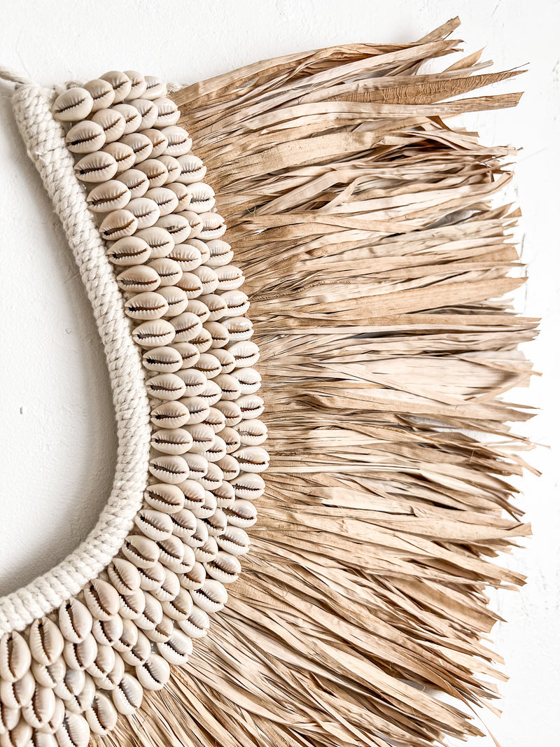 Hand crafted with multiple rows of cowrie shells sewn onto a thick crochet backing with a natural raffia fringe surround. This horseshoe shaped beauty can be hung directly on a wall or from your favourite entrance hook or hanger. Raffia tribal necklace wall hangings for your tropical villa styled interior 