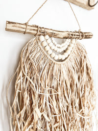 Timber beaded garlands & a waterfall effect of weaved raffia freely cascading from a natural driftwood base.   The Mani wall hanging is a popular choice for use on an entrance wall hook, or filling an empty space around your home. With its raw coastal feel & naturally rustic materials, this hanging is ideal for adding an effortless statement to any interior space. 